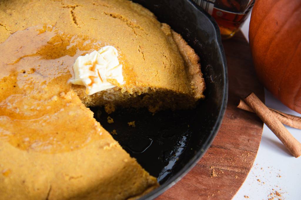 A skillet of cornbread that has a slice taken out of it 