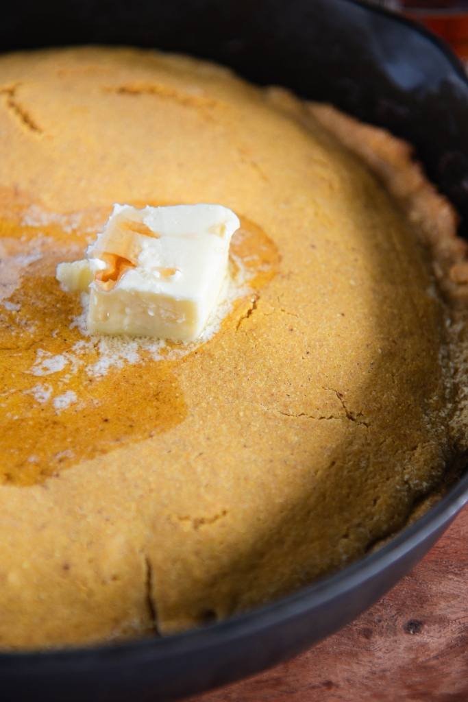 close up of a skillet of cornbread with butter and maple syrup on top 