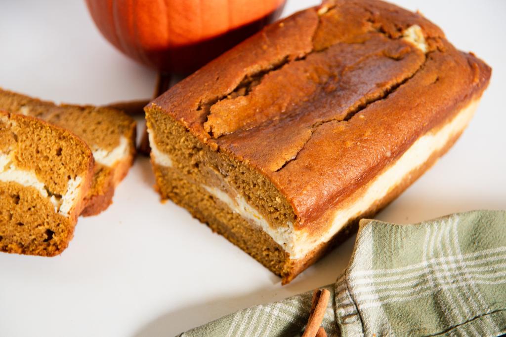 an angled loaf of bread that has a slice cut off it, you can see some slices of bread and pumpkin behind it 