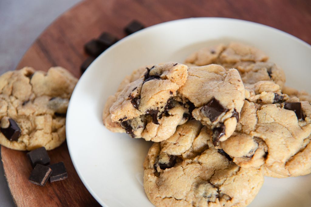 a plate of sourdough cookies, one of them has been broken in half to show the melty chocolate inside