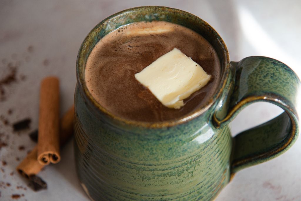 a cup of buttered rum hot chocolate with cinnamon sticks next to it 