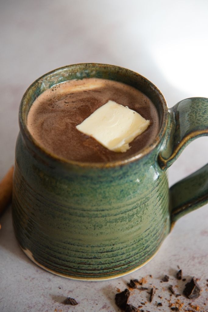 a close up of a cup of hot buttered rum hot chocolate with a pat of butter in it 