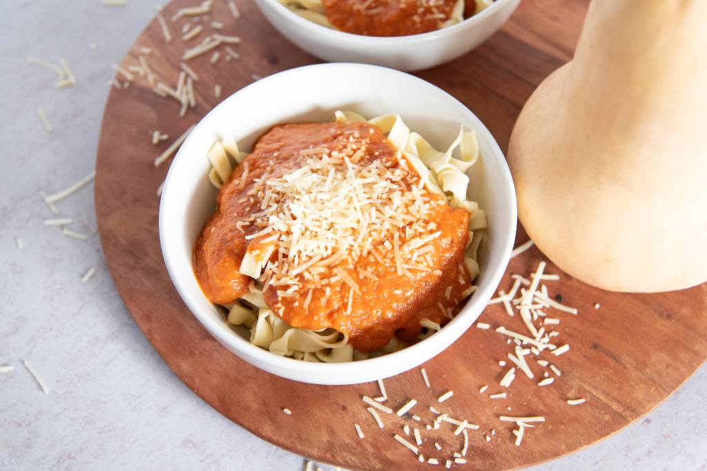 a bowl of noodles with sauce on top, there is another bowl of noodles behind it and a whole butternut squash next to it 