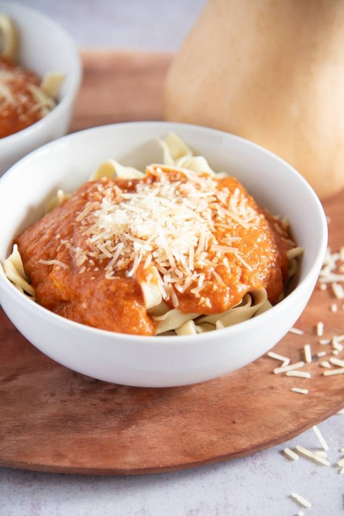 a bowl of noodles with pasta sauce, there is a whole squash behind it 