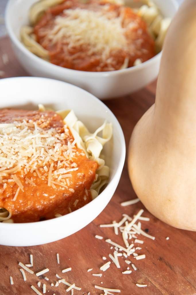 two bowls noodles with sauce, there is also whole butternut squash next to it 