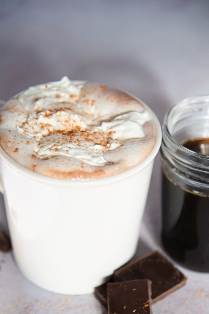 a cup of gingerbread hot chocolate with a jar of gingerbread syrup next to it 