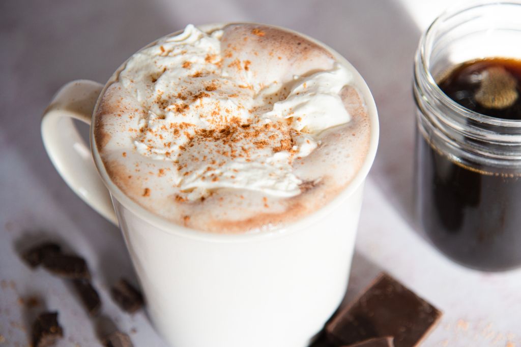a cup of gingerbread hot chocolate, there are pieces of chocolate to the cup, and a jay of syrup.