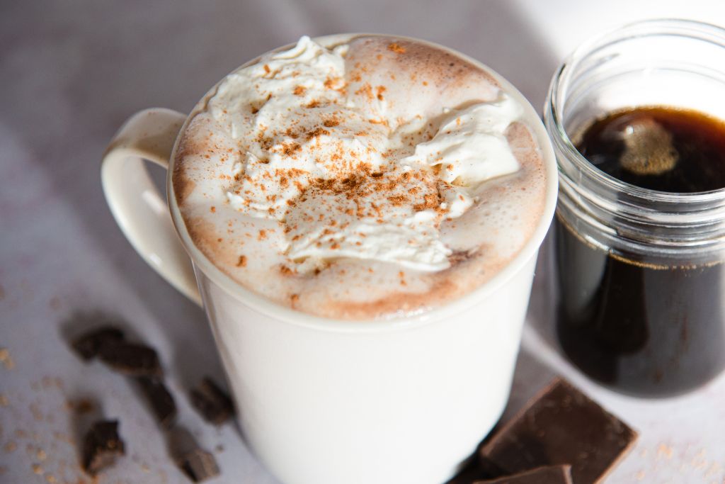 a cup of hot chocolate with a jar of syrup next to it 