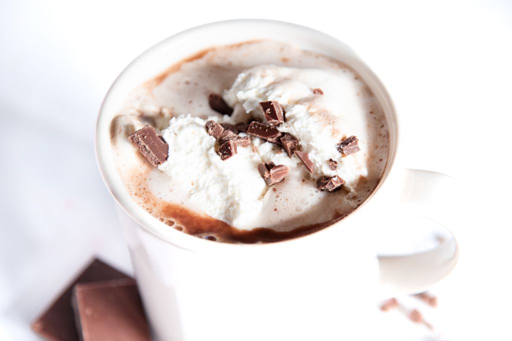 a close up of a cup of hot chocolate with whipped cream and pieces of chocolate on top 