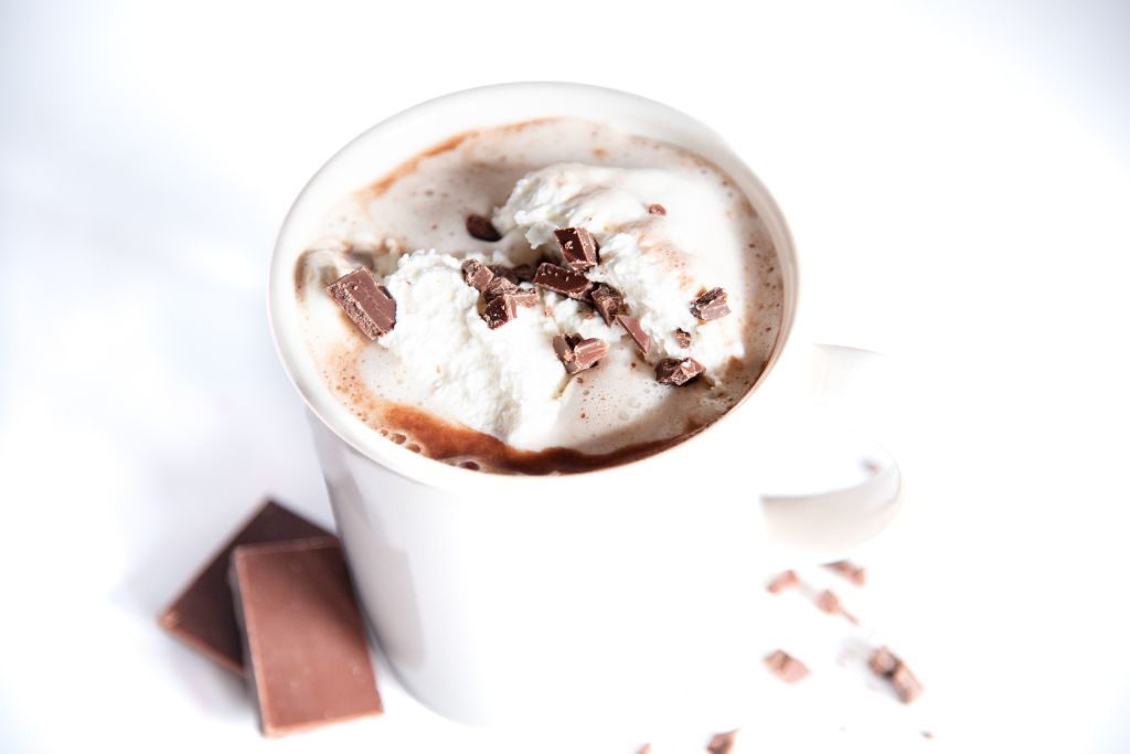 a cup of hot chocolate with whipped cream on top, there also some pieces of chocolate next to the cup