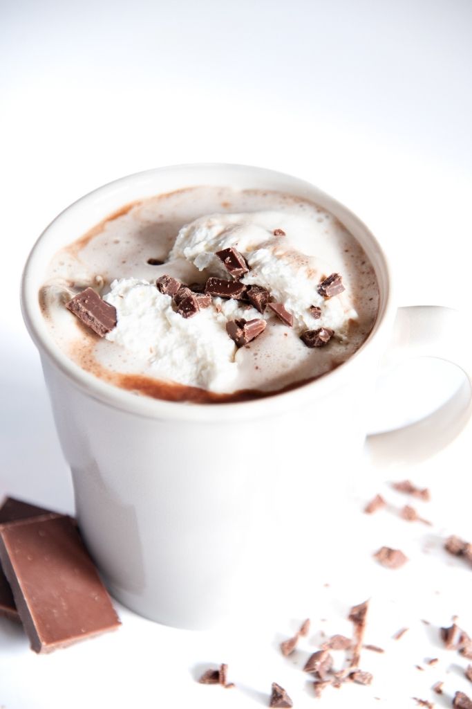 a close up of cup of hot chocolate with whipped cream on top, there are also some pieces of chocolate next to it 