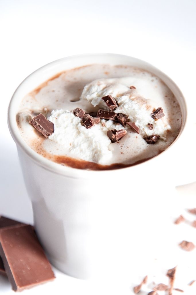 a cup of hot chocolate with whipped cream on top and pieces of chocolate next to it 