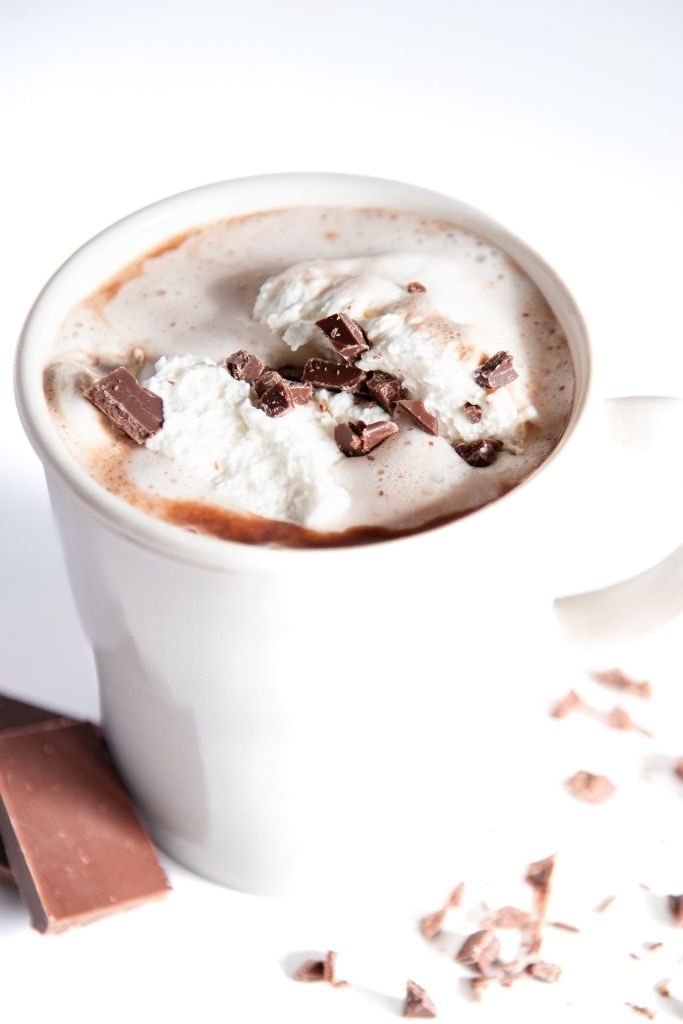 a cup of hot chocolate with whipped cream and chocolate pieces on top 