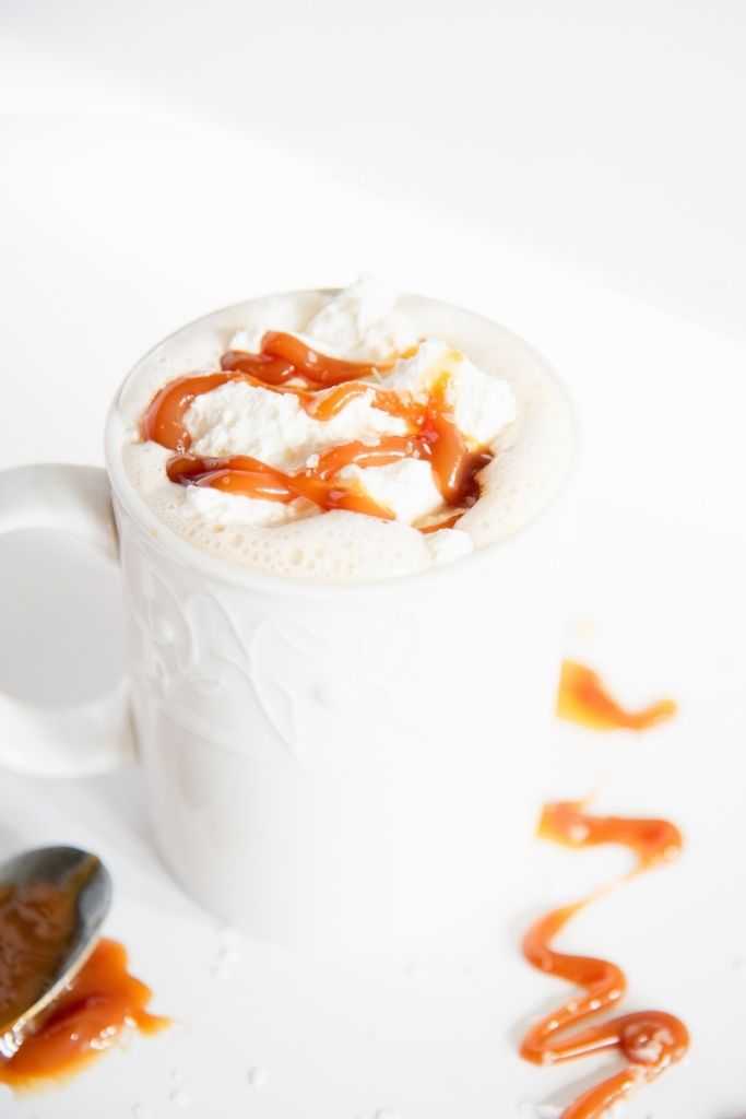 a close up of a finished latte with caramel drizzle next to the cup