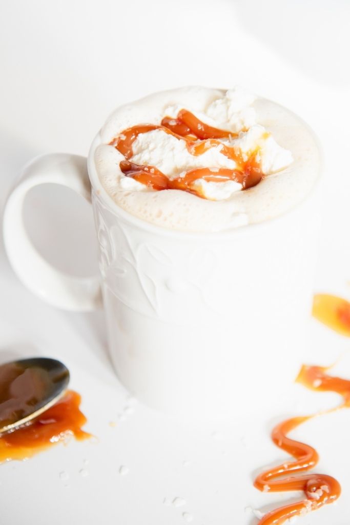 a finished salted caramel latte, there is a drizzle of caramel sauce next to the cup