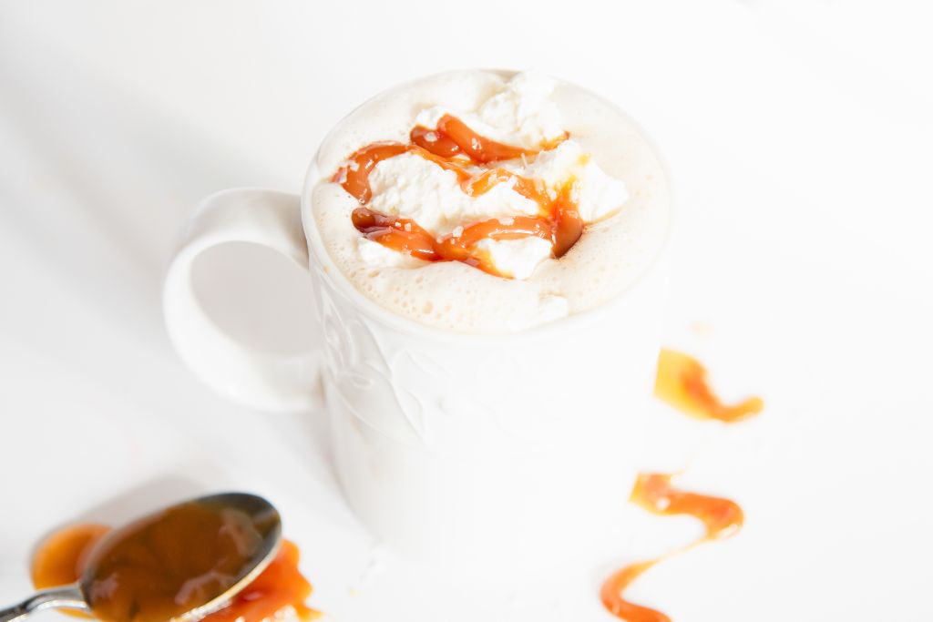 a finished latte with a spoon full of caramel next to it 