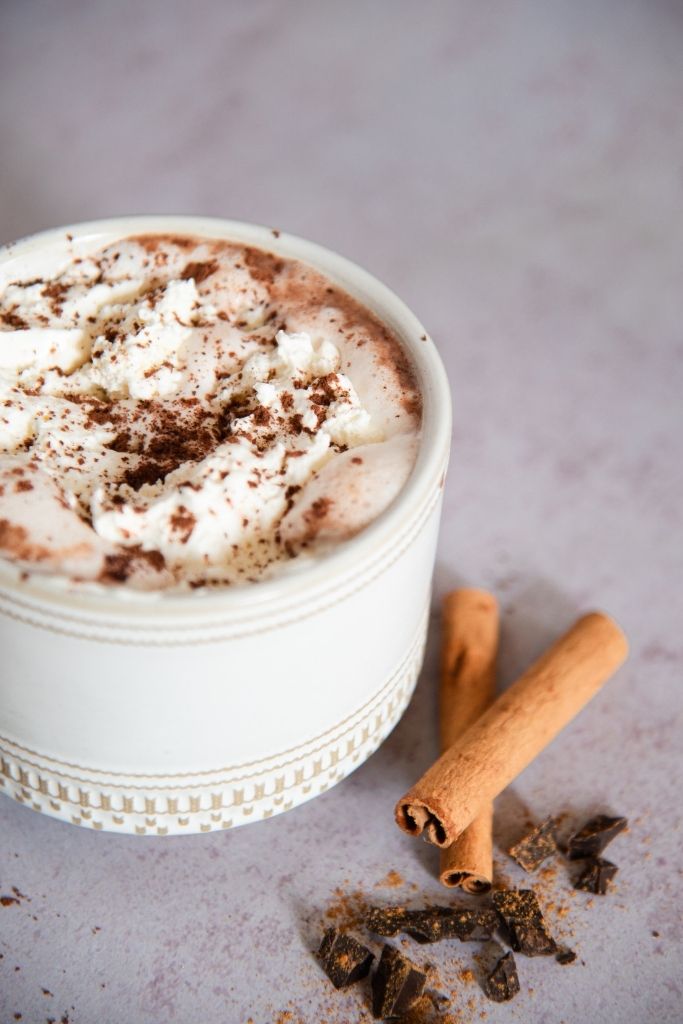 a close up of a mug of hot chocolate with chopped chocolate and cinnamon sticks next to it