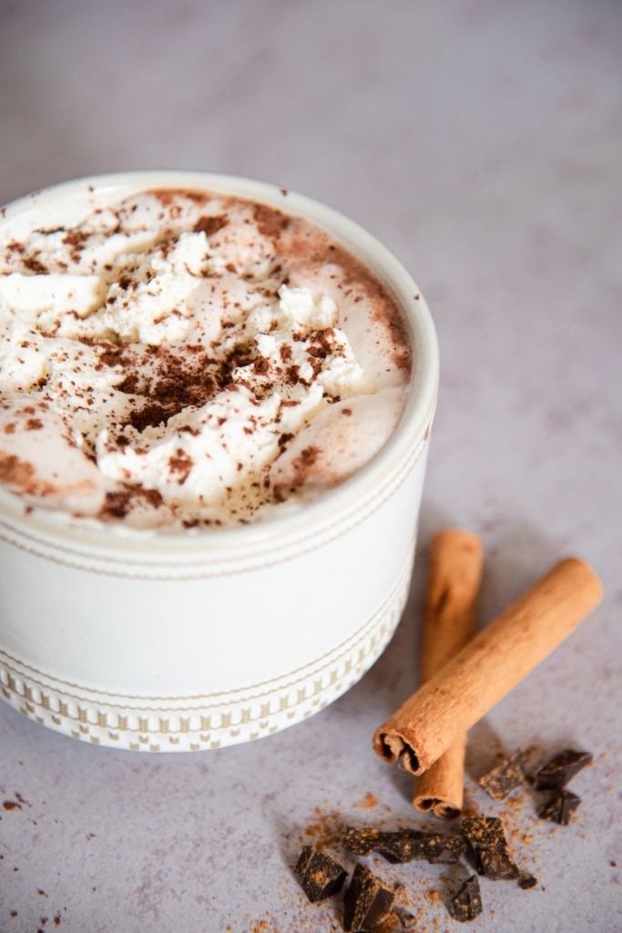 a close up of a mug of chai hot chocolate with cinnamon sticks next to it