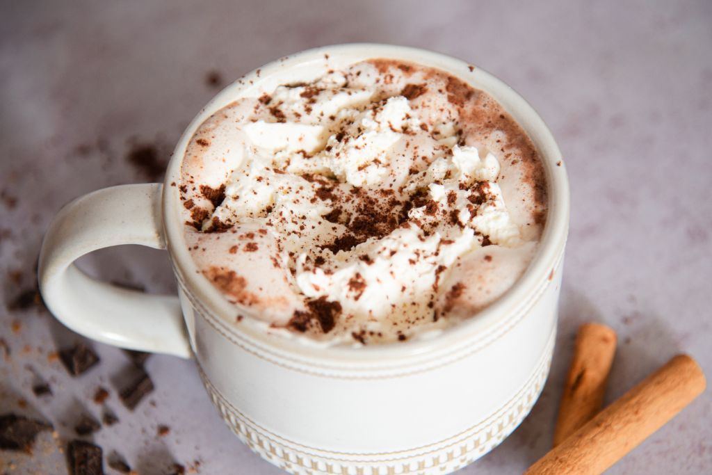 a close up of a mug of chai hot chocolate with cinnamon sticks next to it