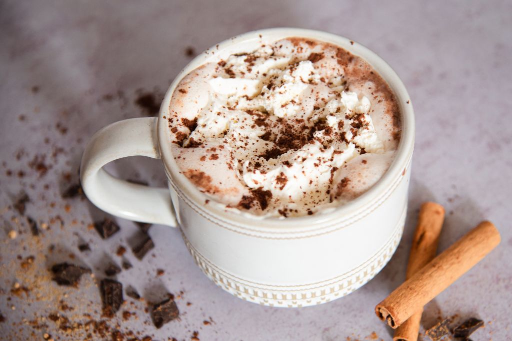a mug of hot chocolate with chopped chocolate and cinnamon sticks around it