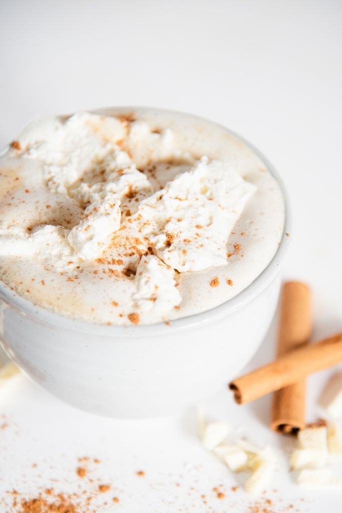 a close up of a cinnabon latte with cinnamon sticks and white chocolate next to it 