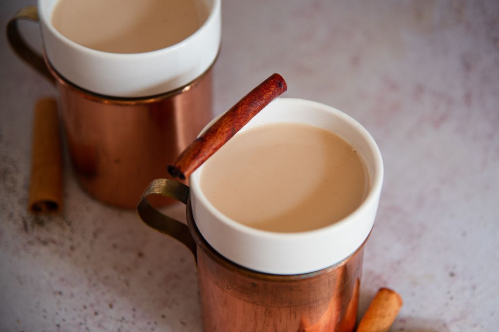 a close up of a bourbon chai nightcap, with a cinnamon stick resting on the edge of the glass