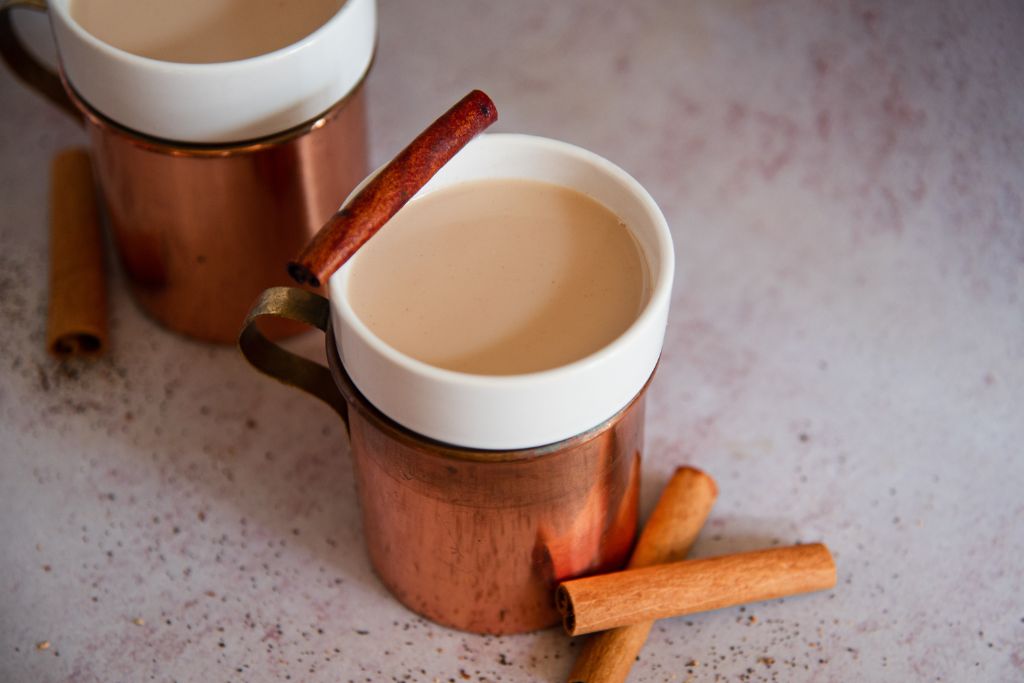 a bourbon chai nightcap with cinnamon sticks next to it, you can see pat of another cup behind it as well