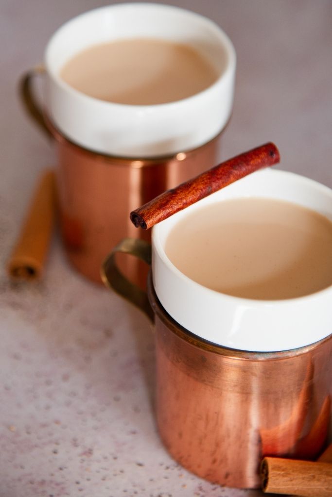 a cut off picture of bourbon chai nightcap, you can see part of another cup and some cinnamon sticks behind it