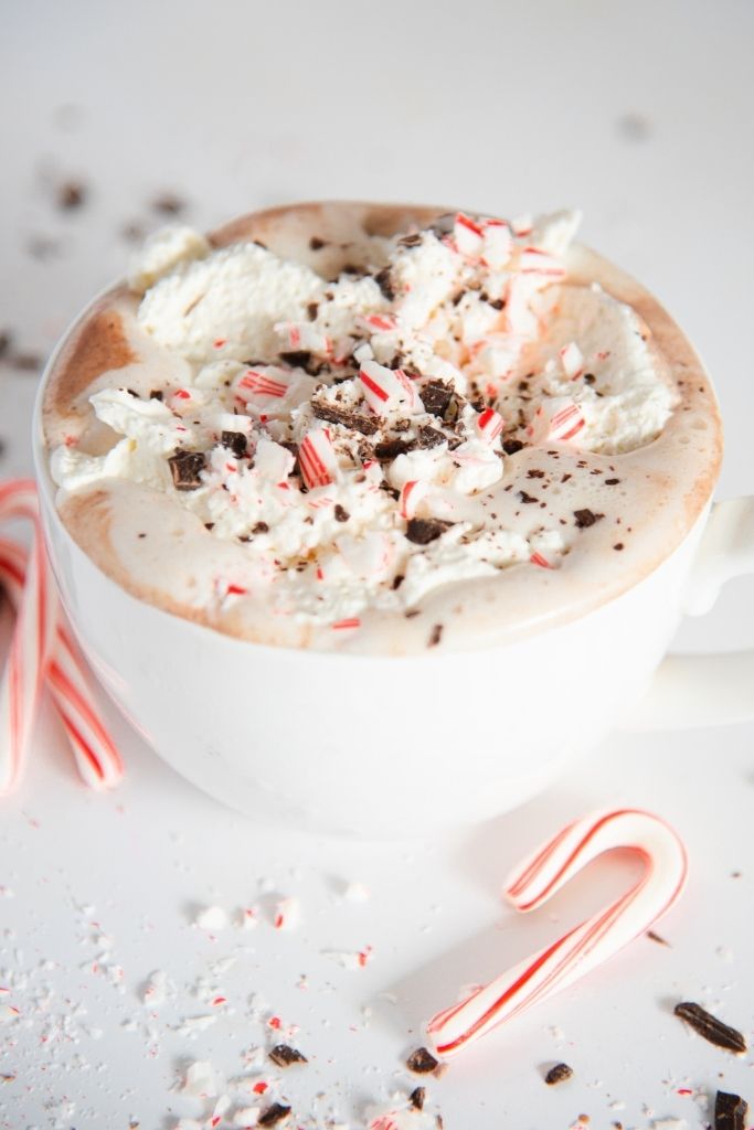 a close up of a cup of hot chocolate topped with whipped cream, candy cane pieces and shaved chocolate 