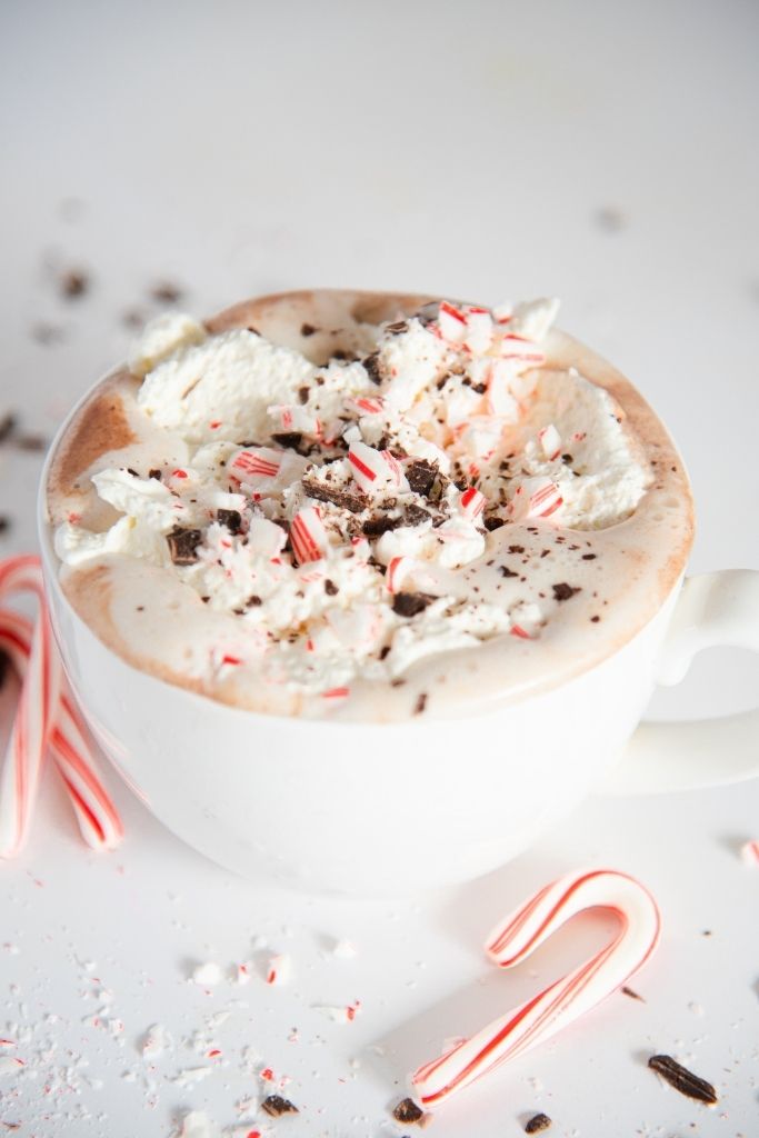 a cup of hot chocolate with whipped cream on top and a mini candy next to it 