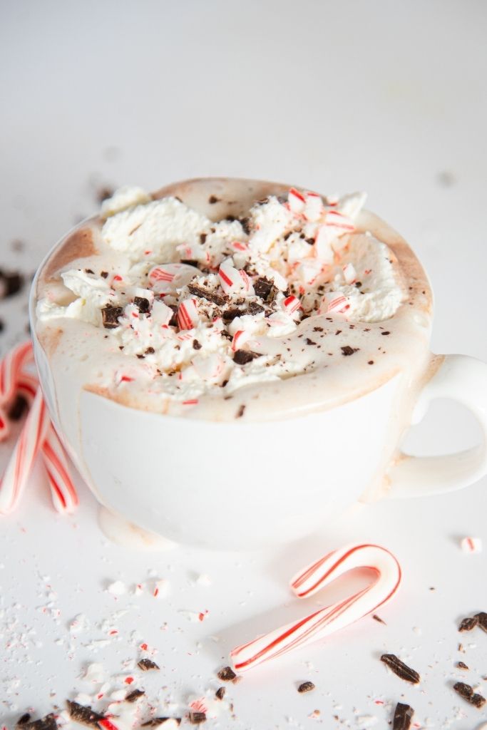 a cup of hot chocolate topped with whipped cream, candy can and chocolate pieces