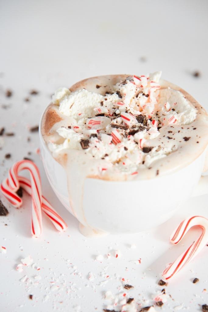 a close up of a cup of hot chocolate with mini candy canes next to it 