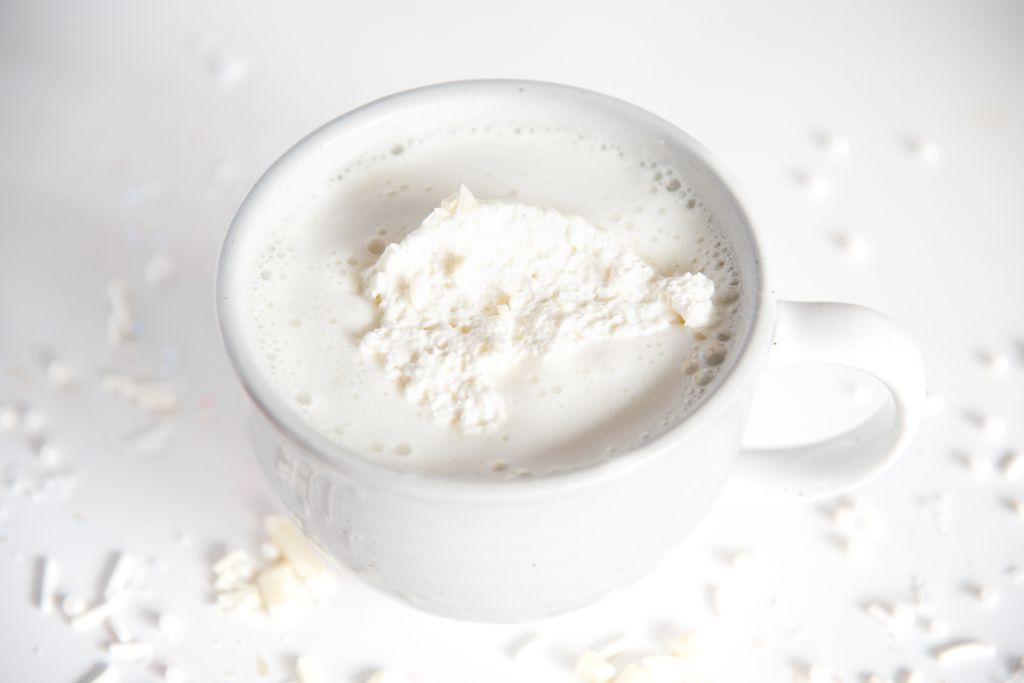 a cup of white hot chocolate with white chocolate sprinkles around it 