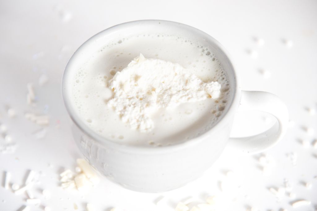 a cup of white hot chocolate with whipped cream on top, there is also chopped white chocolate next to it 
