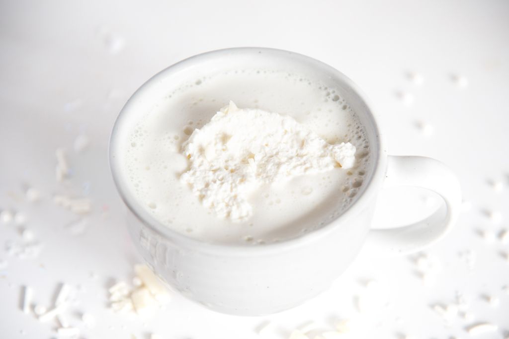 a cup of white hot chocolate with chopped chocolate next to it and whipped cream on top 