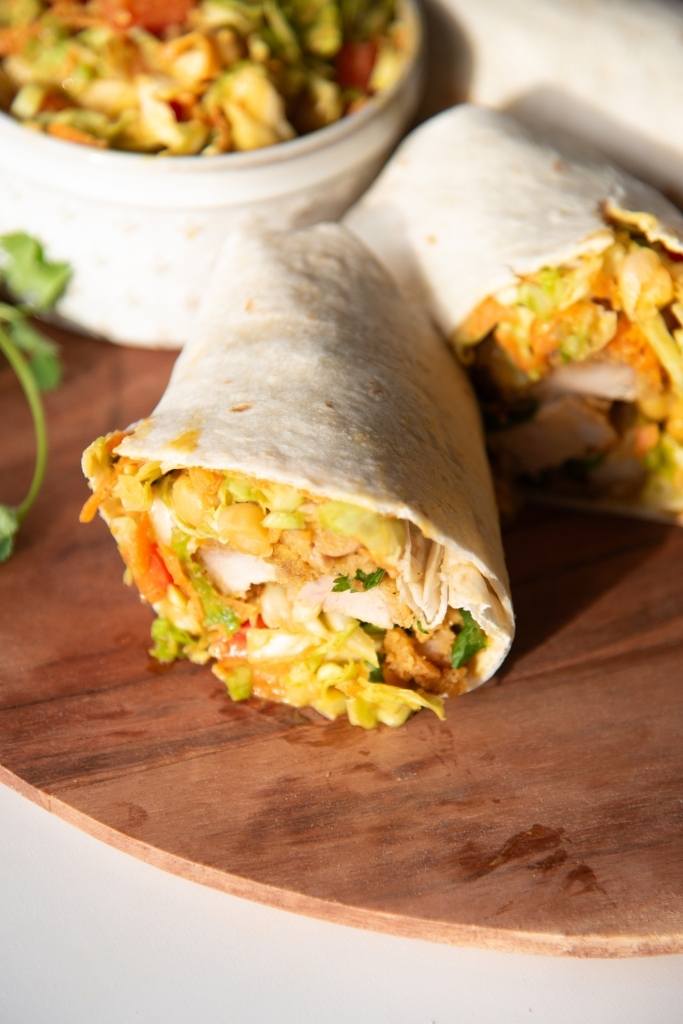 a cut wrap on plate there is a dish of salad next to the wrap