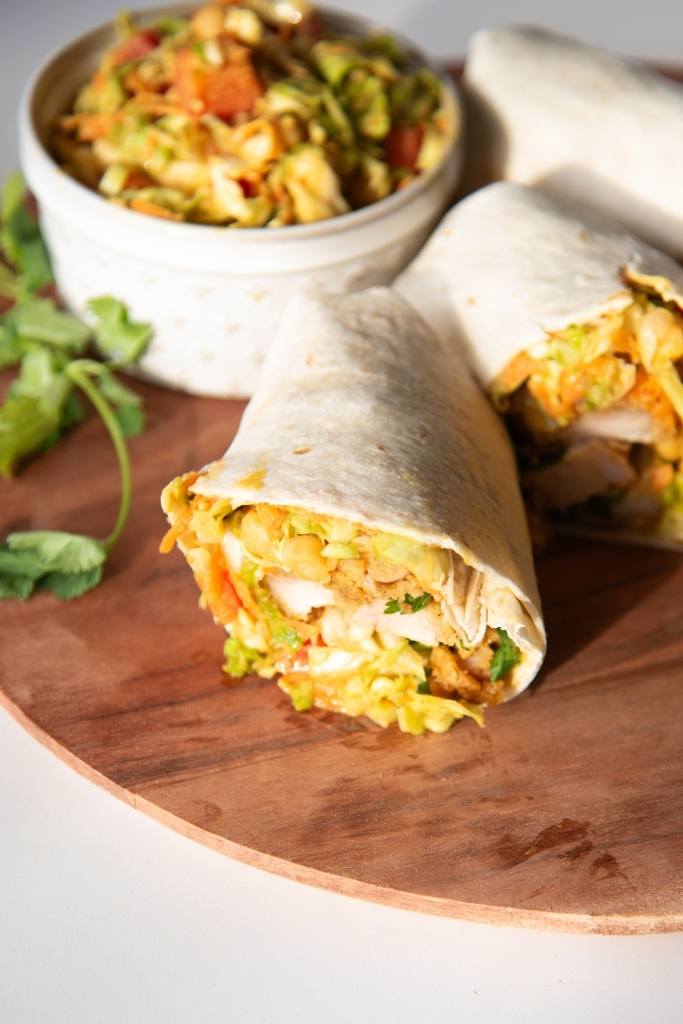 a cut wrap on a plate, there is another wrap and dish of salad behind it