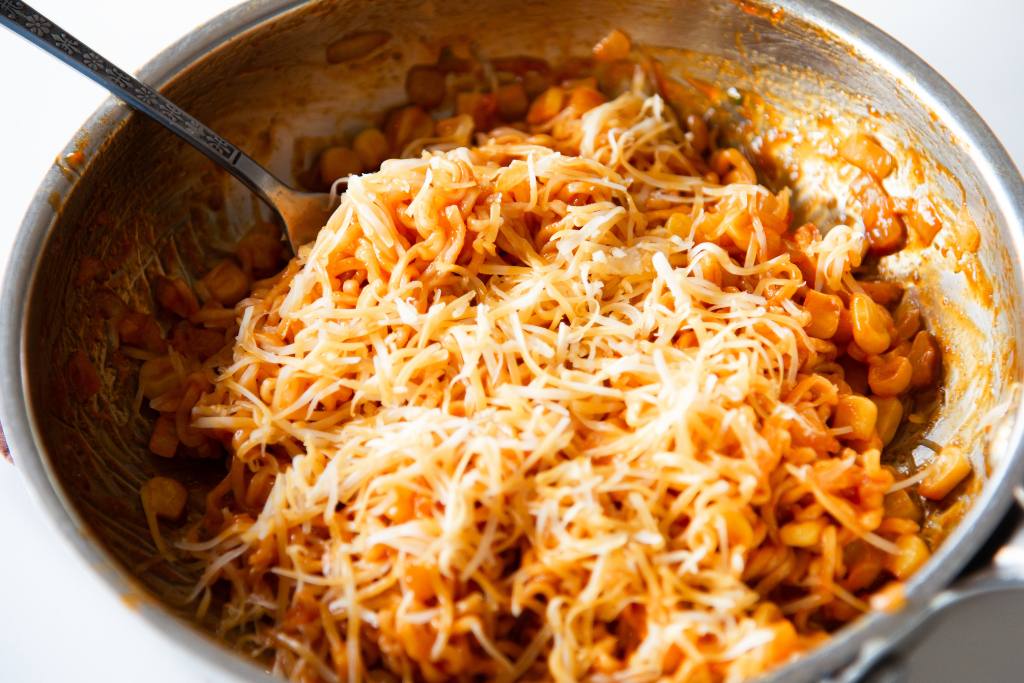 a pan of noodles with cheese on top and fork in it 