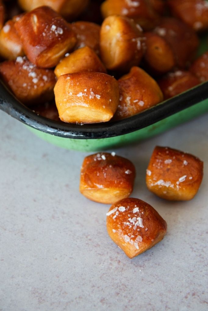 a close up of sourdough pretzel bites, some are in a dish some are on the table next to the dish
