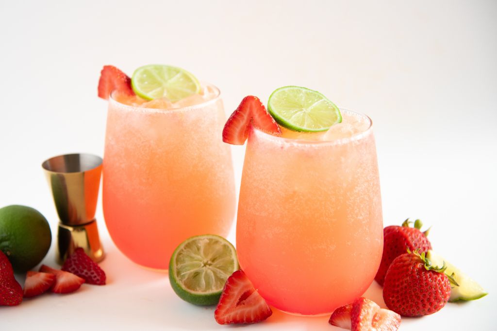 two strawberry mocktails with cut limes and strawberries around them
