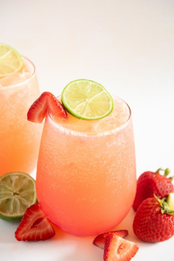 a close up of a strawberry mocktail, with strawberries and a half of a lime next to it