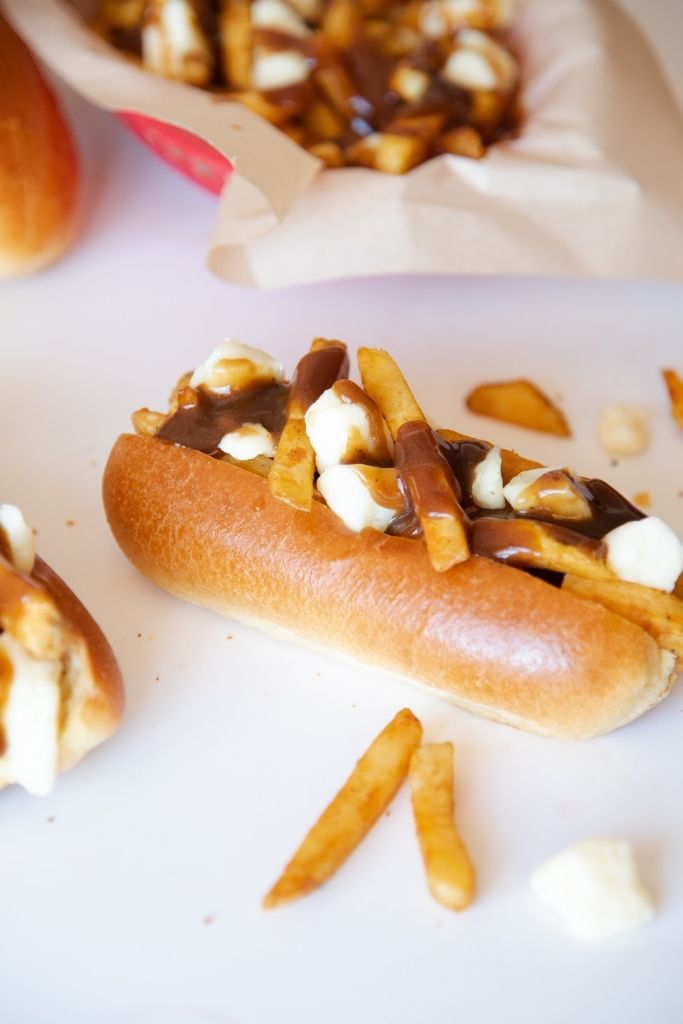 a close up of a hot dog topped with poutine 