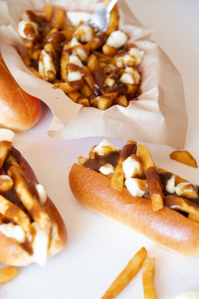 a plate of poutine with poutine topped hot dogs next to it 