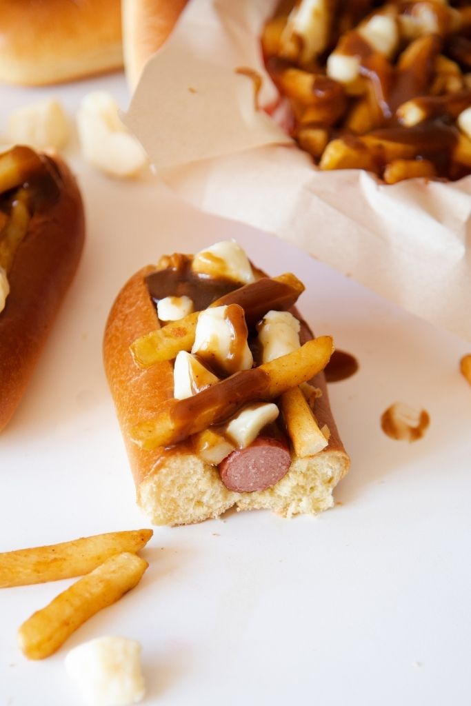 a close up of a poutine topped hot dog that has been cut in half 