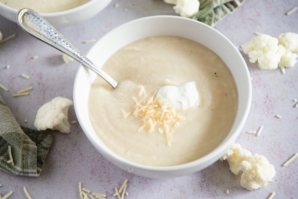 a soup with a spoon in it, and cauliflower pieces around it 