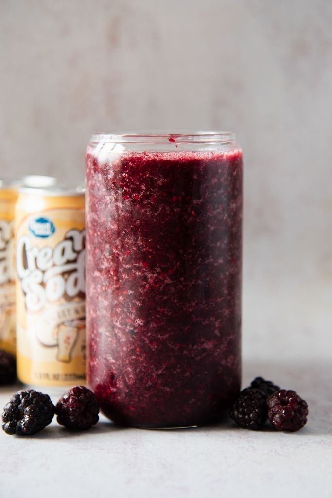 a close up of a blackberry slushy with frozen blackberries around it 