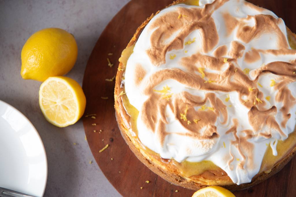 an uncut cheesecake with lemons around it, you can also see part of plate off to one side