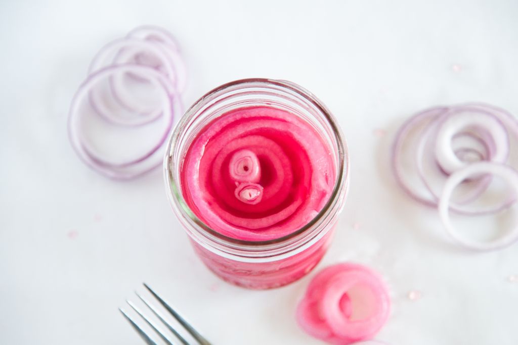 an overhead shot of a jar of pickled red onions, there some onions slices and a fork next to the jar.