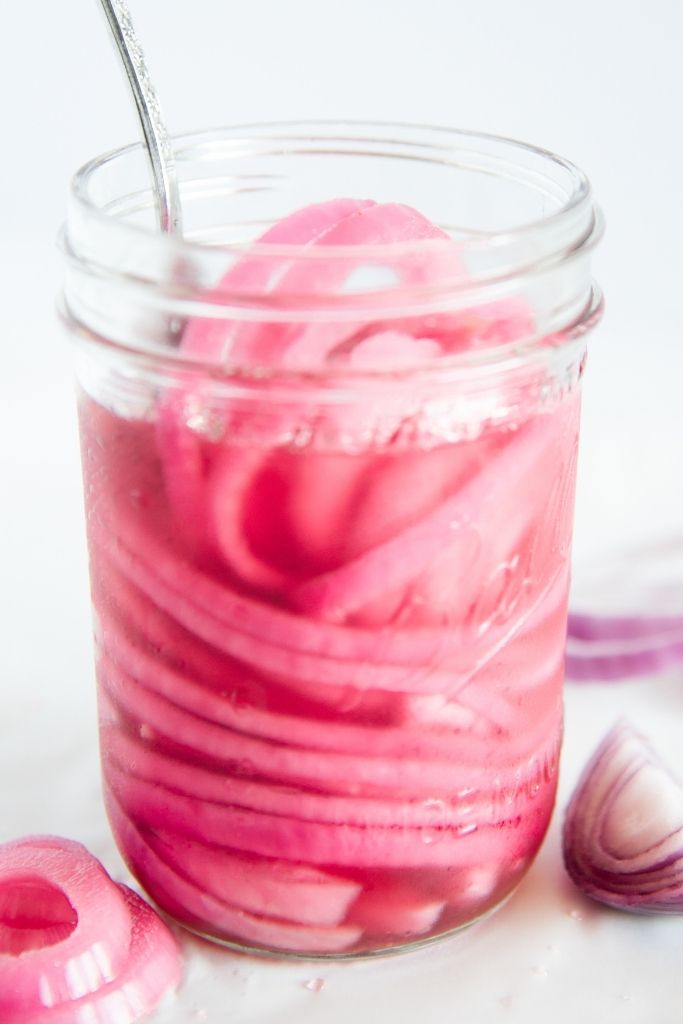 a close up of a jar of pickled onions with a fork stuck in it