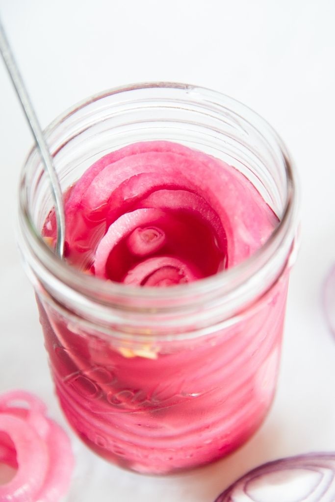 a close up of a jar of pickled onions with a fork in it